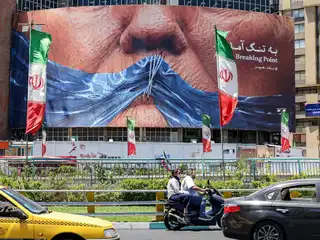 2026 ވަނަ އަހަރުގެ މޭ މަހުގެ 26 ވަނަ ދުވަހު ތެހެރާންގެ ވަލިއަސްރު މައިދާނުގައި، އެމެރިކާގެ ރައީސް ޑޮނަލްޑް ޓްރަމްޕާއި ހުރްމުޒް ކަނޑުއޮޅި ފެންނަ ގޮތަށް ހަރުކޮށްފައިވާ ސިޔާސީ ބިލްބޯޑެއްގެ ކައިރިން ދުއްވާ އެއްޗެހި ދަތުރުކުރަނީ.