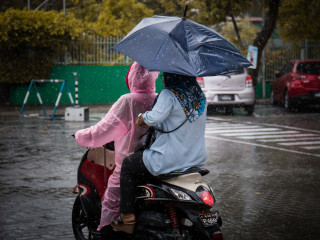 A motorcyclist and her passenger drive through rain on the streets of capital city Malé