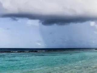 A view of heavy rainfall over the sea just off the coast of an island.