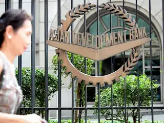 މެނީލާގައި ހުންނަ އޭޝިއަން ޑިވެލޮޕްމަންޓް ބޭންކް (އޭޑީބީ) ގެ މައި އިދާރާގެ ބޭރުގައި ހަރުކޮށްފައިވާ އެ ބޭންކުގެ ލޯގޯ ކައިރިން އަންހެނަކު ހިނގާފައި ދަނީ.