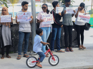 Child on bicycle passing in front of protesters