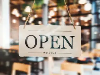 An "Open" sign is displayed on the door of a cafe. | iStock