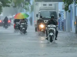A group of people traveling by motorcycle on the streets of Malé amidst heavy rainfall.