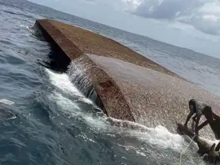 A photograph showing a person atop a previously capsized landing craft.