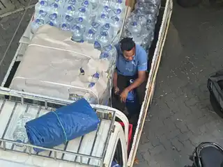 ބިދޭސީ މަސައްކަތްތެރިއަކު ފެން ކޭސްތަކެއް އުފަލަމުންދާ ލޮރީ އެއްގައި ދަތުރުކުރަނީ