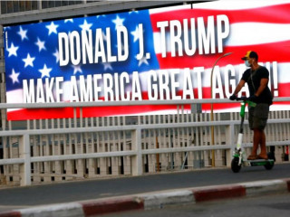 ޓްރަމްޕްގެ ކެމްޕެއިން ބެނާއެއް ކައިރިން މީހަކު މާސްކު އަޅައިގެން ދަނީ