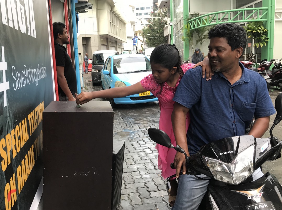 ސެޕްޓެމްބަރު 11، 2017: ދިވެހިރައްޔިތުން ރޮހިންޖާ މުސްލިމުންނާއެކު ޓެލެތޯނަށް އެހީވުމަށް ރާއްޖެ ޓީވީ ކުރިމަތީގައި ބަހައްޓާފައިވާ ފަންޑު ފޮއްޓަށް ކުއްޖަކު ފައިސާ ހަދިޔާކުރަނީ