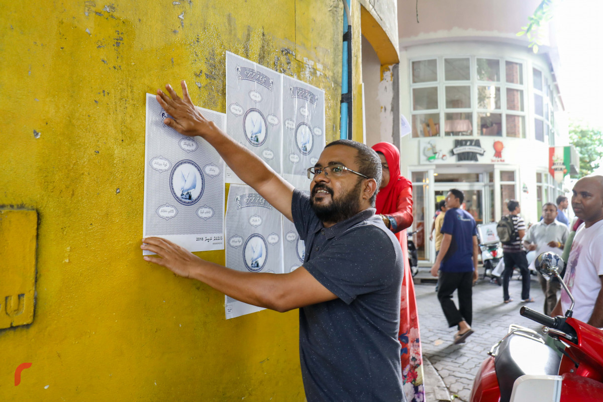 ޖޫން 25، 2018: އެމްޑިޕީއިން "ޖަޒީރާ ރާއްޖެ" ކެމްޕެއިން ޕޯސްޓަރު ހަރުކުރުމަށް ކުރިއަށްގެންދިޔަ ހަރަކާތުގެ ގެއެއްގެ ފާރުގައި ޕޯސްޓަރު ހަރުކުރަނީ، މި ހަރަކާތުގައި މާލޭގެ އެކި ސަރަހައްދުތަކުގައި ޕޯސްޓަރު ހަރުކުރުން ވަނީ ކުރިއަށްގެންގޮސްފައި -- ފޮޓޯ: މުހައްމަދު ޝަރުހާން / ރާއްޖެ އެމްވީ