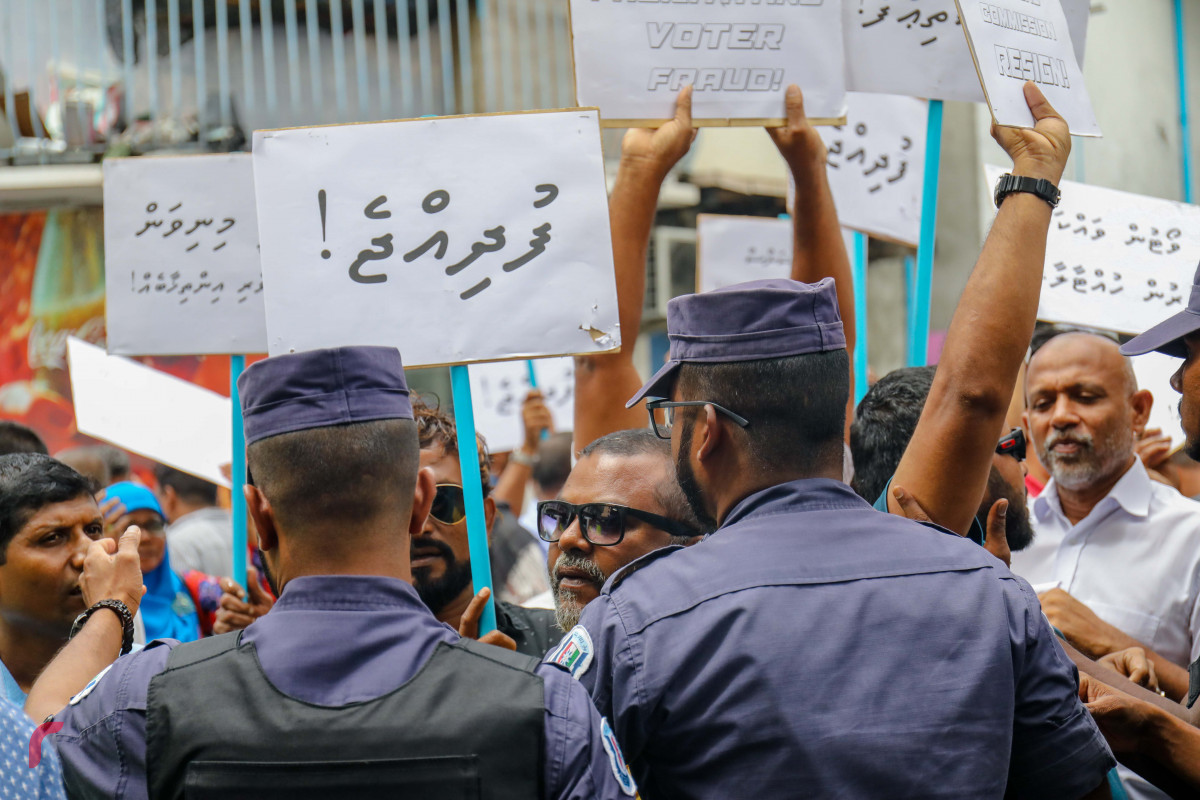ޖުލައި 23، 2018: އިލެކްޝަންސް ކޮމިޝަނުގެ ރައީސް އަހުމަދު ޝަރީފު އިސްތިއުފާދިނުމަށާއި މިނިވަން އިންސާފުވެރި އިންތިހާބެއް ބޭއްވުމަށް ގޮވާލައި އިލެކްޝަންސް ކޮމިޝަނުގެ އޮފީސް ހުރި ސަރަހައްދުގައި ގުޅިފައިވާ އިއްތިހާދުގެ މެމްބަރުން ކުރި މުޒާހަރާ ރޫޅާލުމަށް ފުލުހުން ހަރަކާތްތެރިވަނީ، މި އެއްވުމުގައި މިނިވަން އިންތިހާބަކަށް ގޮވާލައި ޝުއޫރު ފާޅުކޮށްފައިވާ ބޯޑު ފަދަ ތަކެތި ވަނީ ބޭނުންކޮށްފައި-- ފޮޓޯ: މުހައްމަދު ޝަރުހާން / ރާއްޖެ އެމްވީ