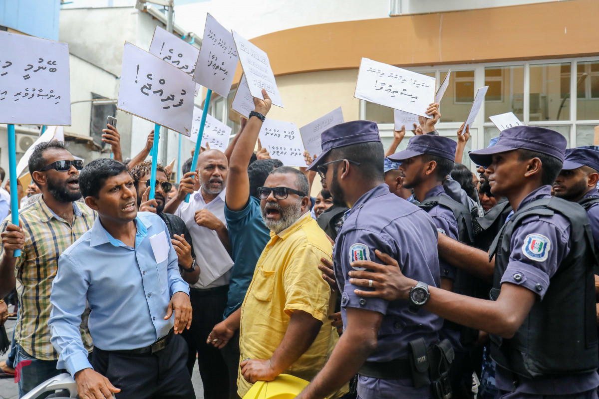 ޖުލައި 23، 2018: އިލެކްޝަންސް ކޮމިޝަނުގެ ރައީސް އަހުމަދު ޝަރީފު އިސްތިއުފާދިނުމަށާއި މިނިވަން އިންސާފުވެރި އިންތިހާބެއް ބޭއްވުމަށް ގޮވާލައި އިލެކްޝަންސް ކޮމިޝަނުގެ އޮފީސް ހުރި ސަރަހައްދުގައި ގުޅިފައިވާ އިއްތިހާދުގެ މެމްބަރުން ކުރި މުޒާހަރާ ރޫޅާލުމަށް ފުލުހުން ހަރަކާތްތެރިވަނީ، މި އެއްވުމުގައި މިނިވަން އިންތިހާބަކަށް ގޮވާލައި ޝުއޫރު ފާޅުކޮށްފައިވާ ބޯޑު ފަދަ ތަކެތި ވަނީ ބޭނުންކޮށްފައި-- ފޮޓޯ: މުހައްމަދު ޝަރުހާން / ރާއްޖެ އެމްވީ