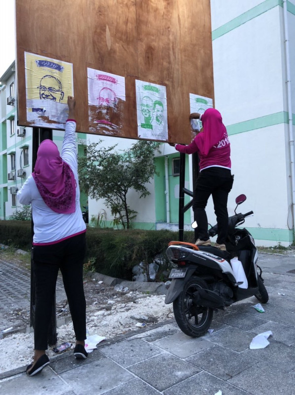 ރައީސް ޔާމީން 2018 ޖަހާފައިވާ ޓީޝާޓްތަކެއް ލައިގެން ތިބި ބަޔަކު ކޯލިޝަންގެ ޕޯސްޓަރުތައް ނައްޓުވަނީ