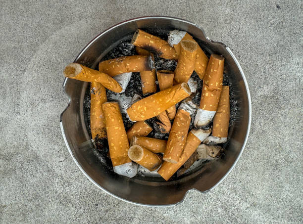 A ashtray full of discarded cigarette butts, with ash scattered on the table