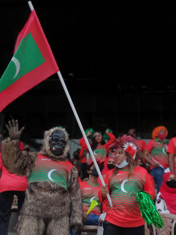 "މަހިންދަ ރާޖަޕަކްސަ ޓްރޮފީ" ފުޓްބޯޅަ މުބާރާތުގައި ދިވެހިރާއްޖެ އާއި ސްރީލަންކާ ބައްދަލުކުރާ މެޗުގައި، ދިވެހި ޓީމަށް ހިތްވަރު ދިނުމަށް ދަނޑަށް ވަދެ ތިބި ދިވެހި ސަޕޯޓަރުން - ފުޓްބޯޅައިގެ ފޯރި ނެގުމަށް ދިވެހި ސަޕޯޓަރެއް ޚާއްސަ ހެދުމެއްގައި، މިއީ ލަންކާގައި ދިރިއުޅޭ ދިވެއްސެއް އަމިއްލަ އަށް ފަހާފައިވާ ހެދުމެއް - ފޮޓޯ: މުޙައްމަދު ފައިސަލް