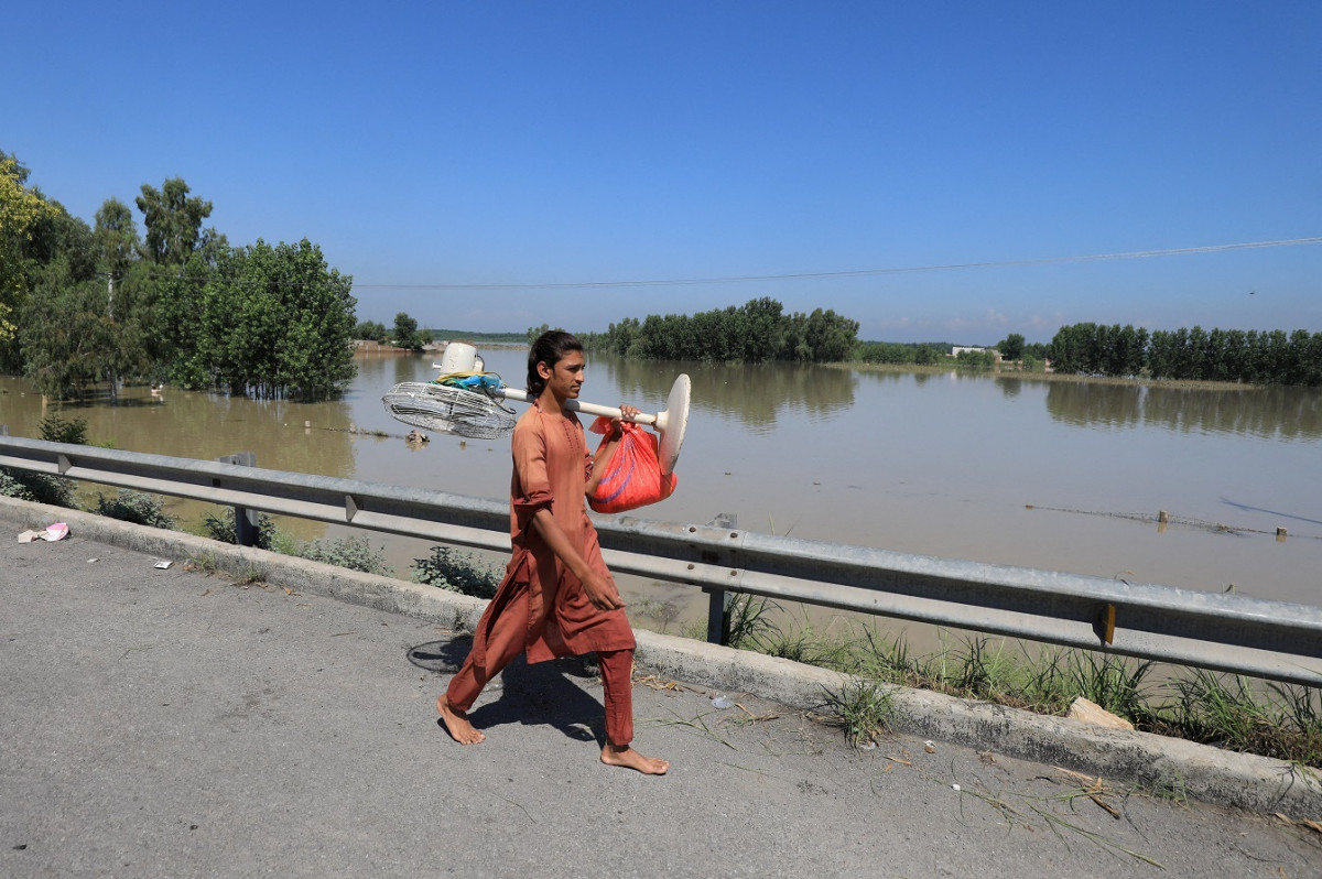 ޕާކިސްތާނުގެ ޗާރްސަދާގައި ހުޅަނގު މޫސުމުގެ ވިއްސާރައާއި ފެންބޮޑުވުމުގެ ސަބަބުން އުފެދިފައިވާ ޗަކަގަނޑެއް ތެރޭގައި މީހަކު ފަންކާއެއް ހިފައިގެން ދަނީ - ފޮޓޯ: ރޮއިޓަރސް