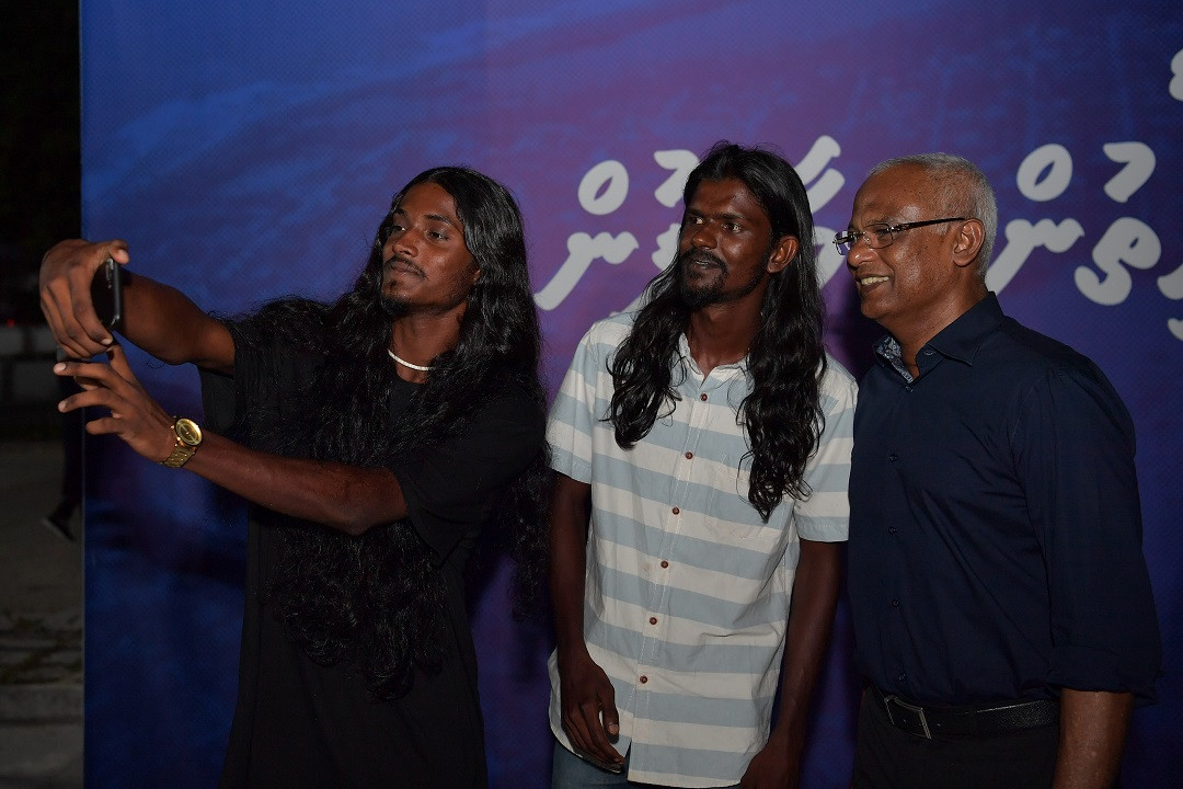 ރައީސުލްޖުމްހޫރިއްޔާގެ ދެކަނބަލުން އައްޑޫ ސިޓީގެ ރައްޔިތުންނަށް ދެއްވި މާހެފުން -  ދެ ޒުވާނަކު ރައީސައެކު ފޮޓޯއެއް ނަގަނީ - ފޮޓޯ: ރައީސް އޮފީސް