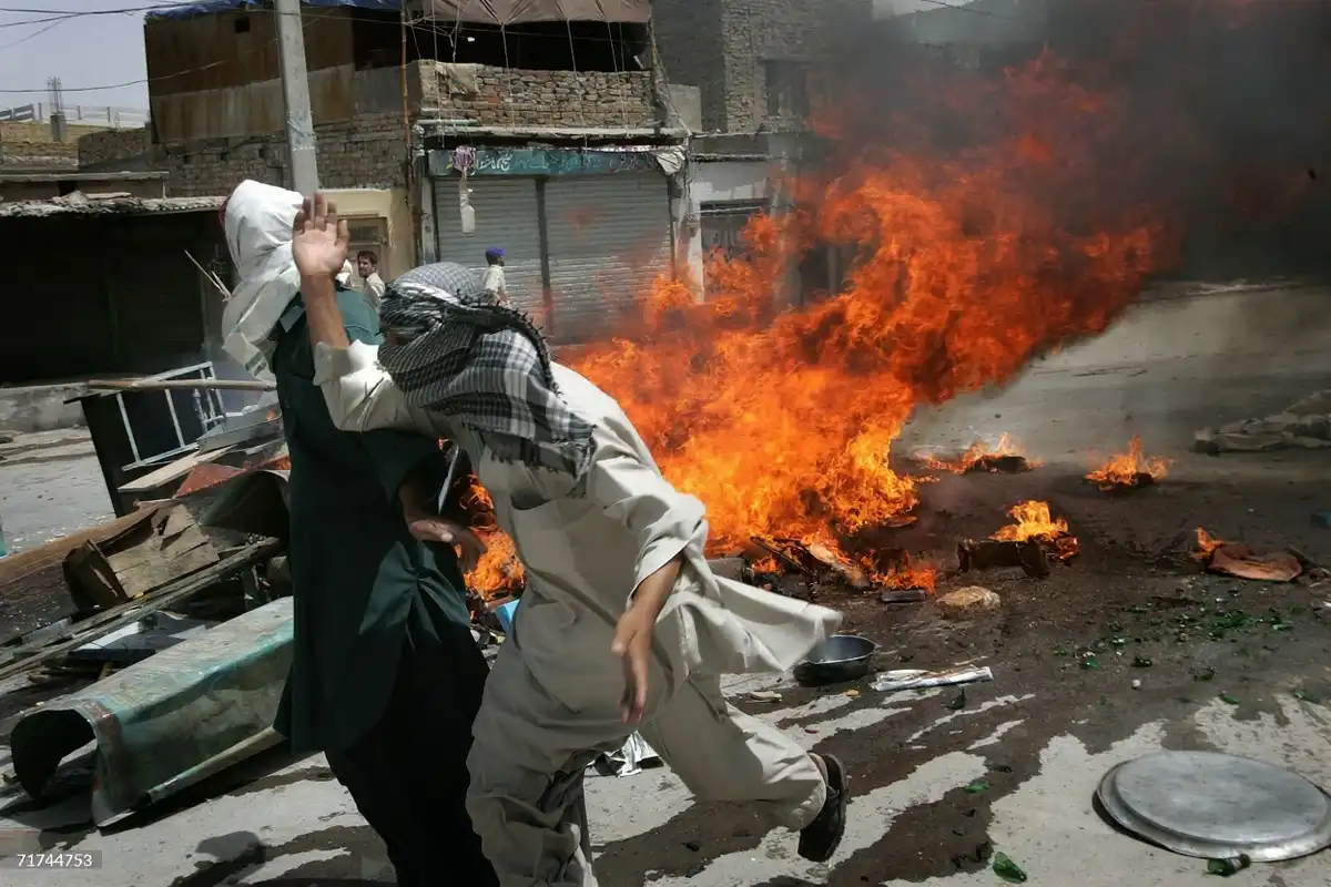 ޕާކިސްތާނުގެ ކުއެޓާގައި 2006 ވަނަ އަހަރުގެ އޮގަސްޓް މަހުގެ 29 ވަނަ ދުވަހު ކުރިއަށްދިޔަ ހަމަނުޖެހުން ބޮޑު މުޒާހަރާއެއްގެ ތެރޭގައި، ރޯކޮށްލާފައިވާ ކުނިތަކެއްގެ ކައިރިން ހަމަނުޖެހުން ހިންގާ މީހުން ދުވެފައި ދަނީ.