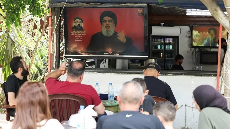 ލުބުނާނުގެ ދެކުނުގެ ޓަޔާގެ ކެފޭއެއްގައި ލުބުނާނުގެ ހިޒްބުالله ލީޑަރު ހަސަން ނަސްރުالله ތަގުރީރު ކުރައްވާ މަންޒަރު ފެންނަ ބްރޯޑްކާސްޓެއް ރައްޔިތުން ބަލަނީ