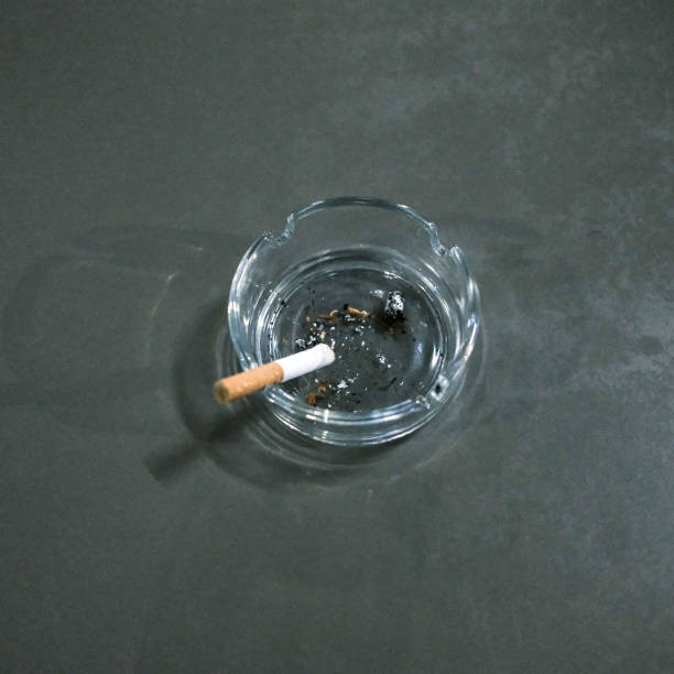 A glass ashtray containing ashes and a partially smoked cigarette